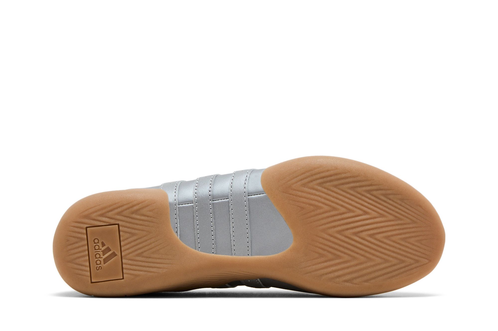 Tênis feminino Adidas Wmns Taekwondo Mei Ballet prata metálico visto de baixo, com sola de borracha marrom com padrão de linhas em zig-zag e logo Adidas em um dos calcanhares. Fundo branco.