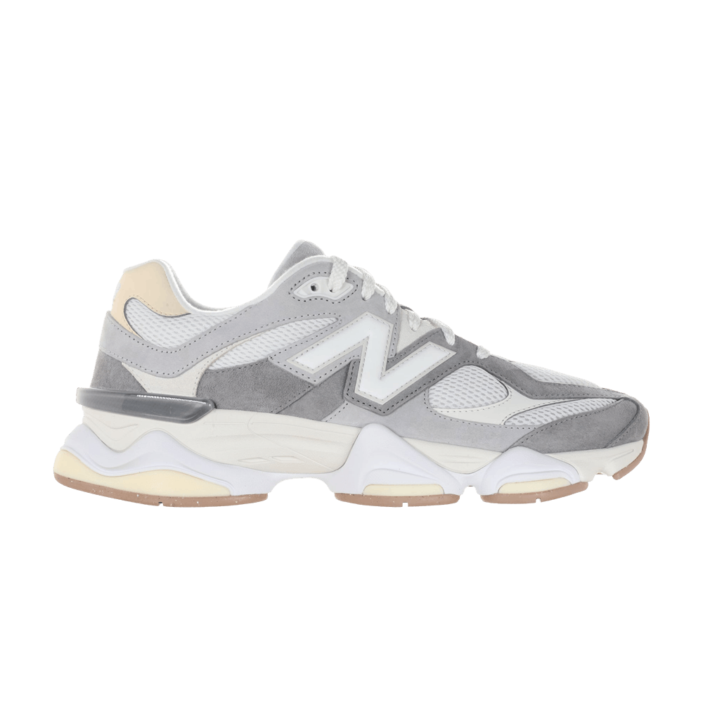 Tênis New Balance modelo 9060 na cor cinza slate, com design moderno e sofisticado. A parte superior é feita de materiais texturizados em tons de cinza claro e escuro, com detalhes em bege. O tênis está posicionado de lado, em um fundo neutro. A legenda 'N' em destaque na lateral, destacando a marca.